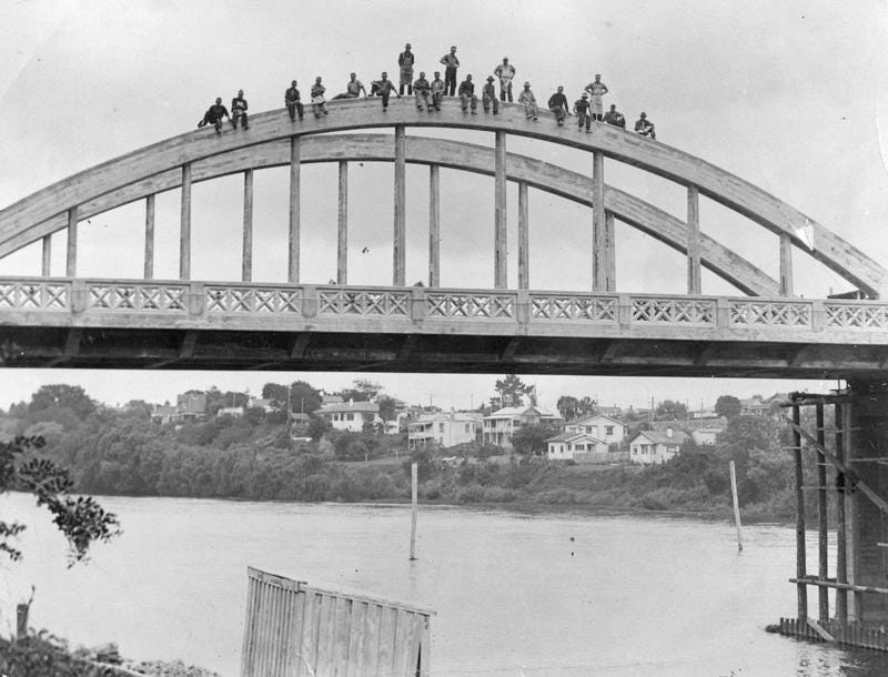 An old black and white photograph of workmen standing and sitting on top of one of the arches of the Fairfield Bridge.