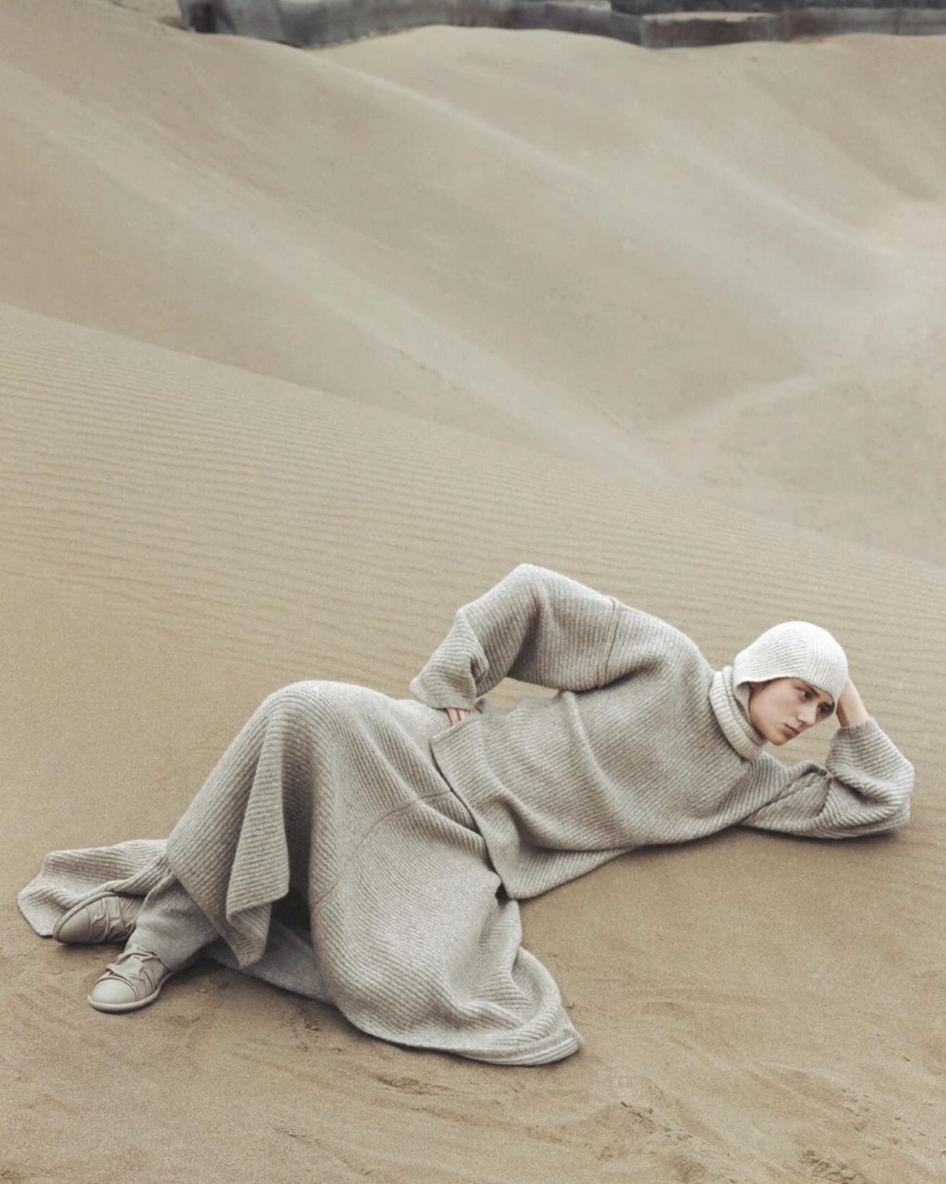 Woman wearing knitwear and balaclava lying in a sand dune.