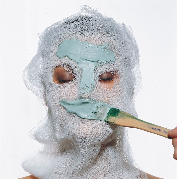 This may contain: a woman wearing a white mask and holding a paintbrush to her face