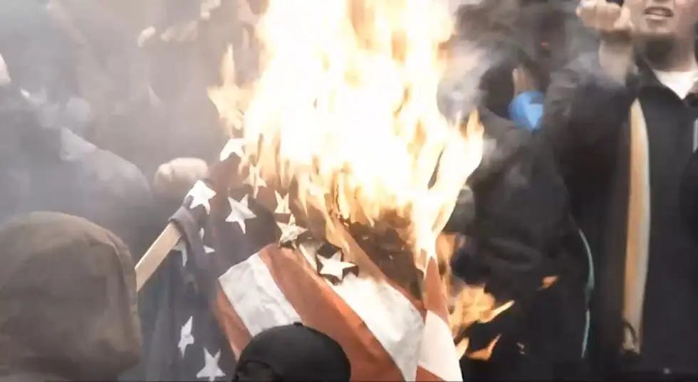 A group of people is observing the burning of an American flag