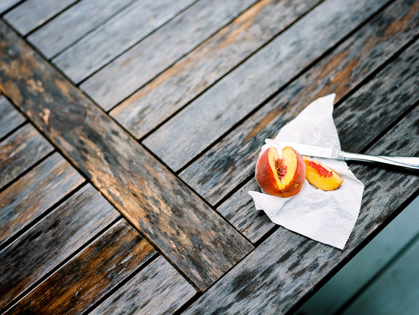 Photo of a sliced-open peach on a wooden table outdoors