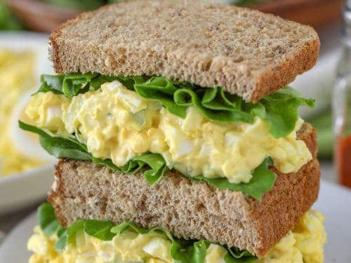 two halves of an egg salad and lettuce sandwich stacked on top of each other