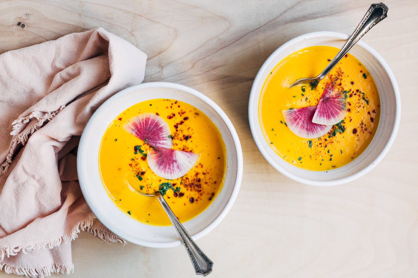 Two bowls of sweet potato soup topped with herbs and radishes.