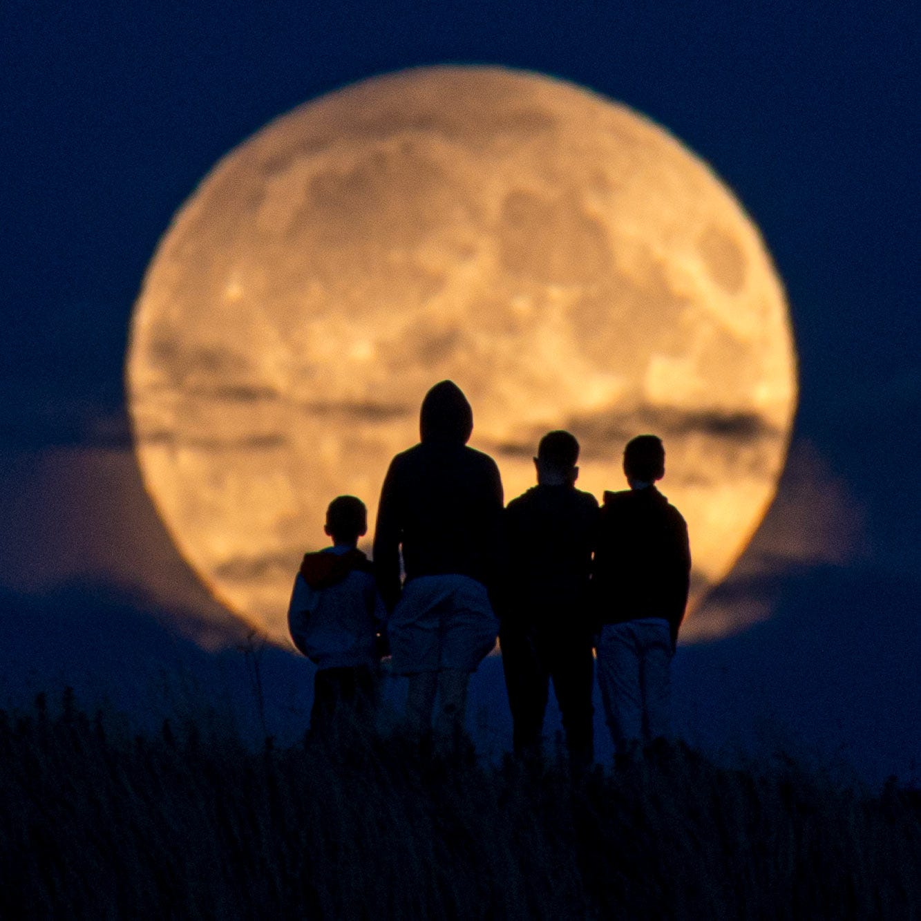 A huge moon in the distance with 4 people silhouetted in front of it staring at it