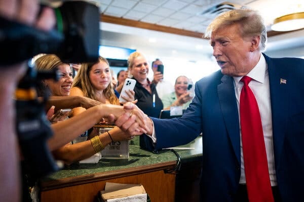 Donald Trump behind a counter shaking hands with well-wishers.