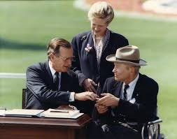photo of justin dart, a white republican dude in a wheelchair and cowboy hat, shaking hands with George HW BUsh at the signing of the ADA