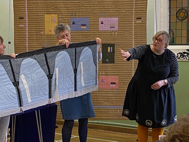 A woman is talking about a quilt featuring figures stitched in.