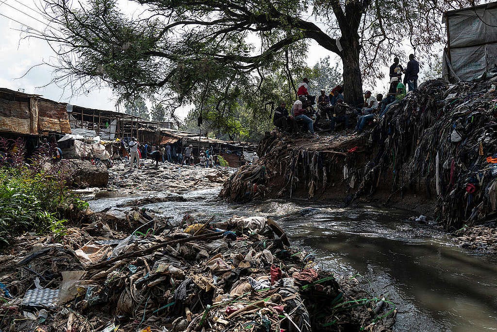 Image of the clooged-up Nairobi River through the Gikomba market in Kenya. The photo shows the banks of the water stream covered in waste. Very little parts of the ground can be seen through the amount of waste. 