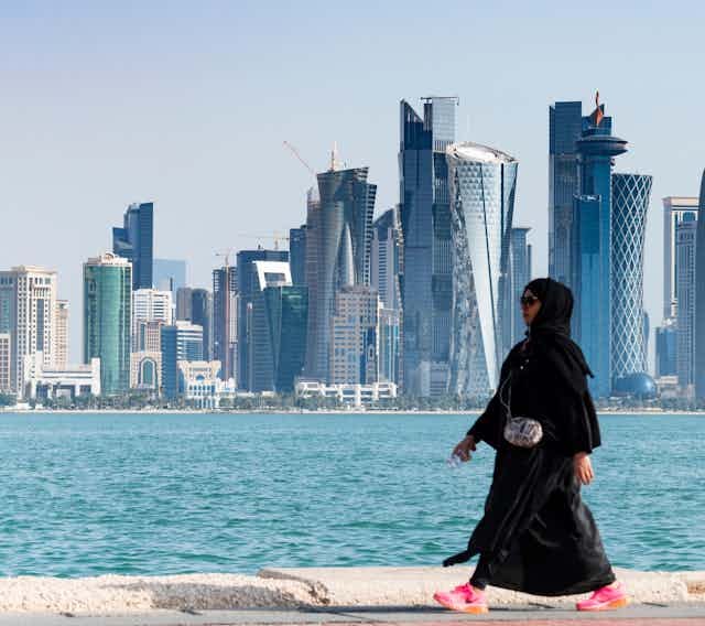 A woman walking along the waterfront with the Doha city skyline in the background.