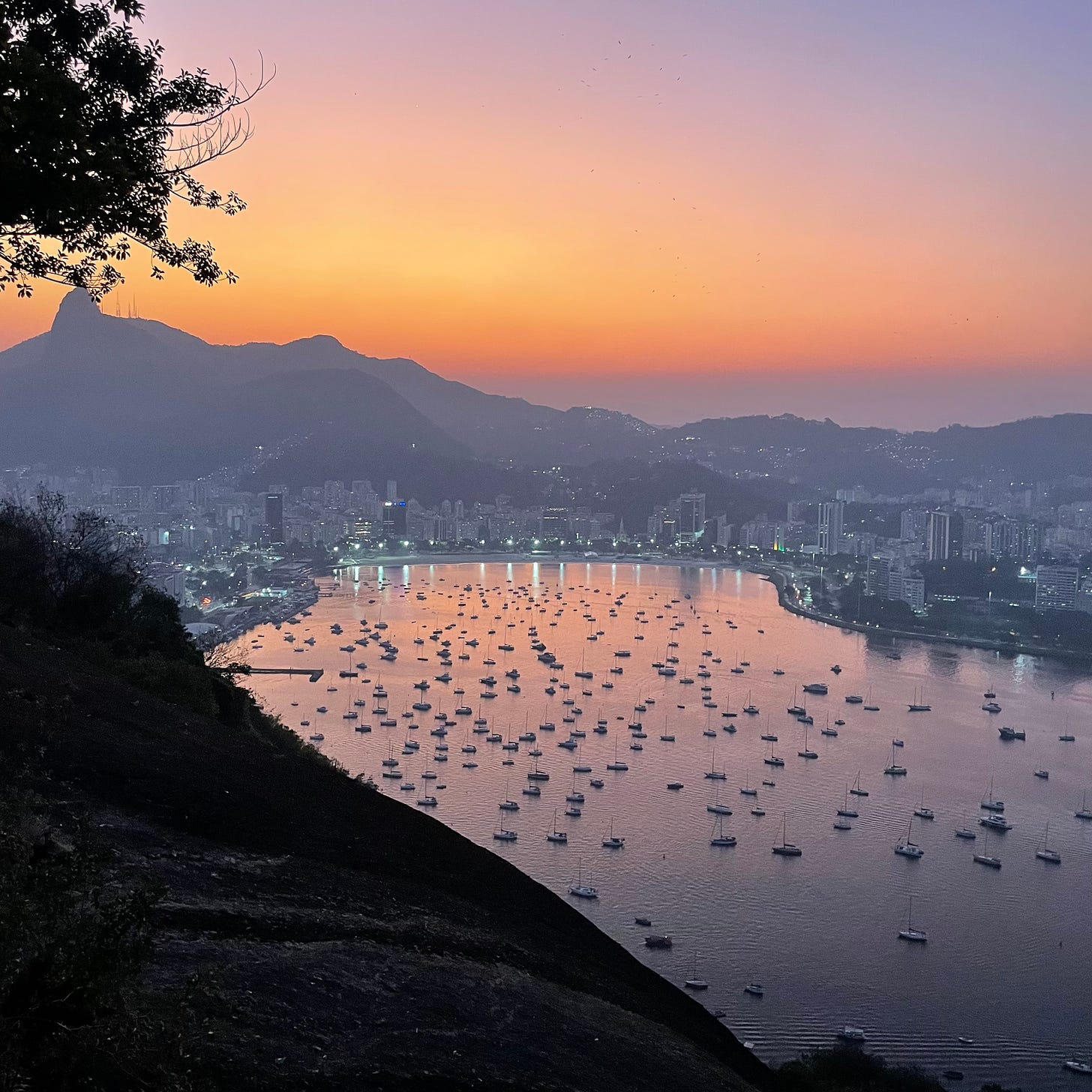 A picture of a stunning orange sunset over mountains and reflected in a harbor. Rio de Janeiro is visible all around.