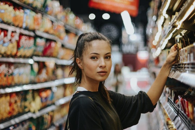 A woman in a supermarket, picking something off a shelf