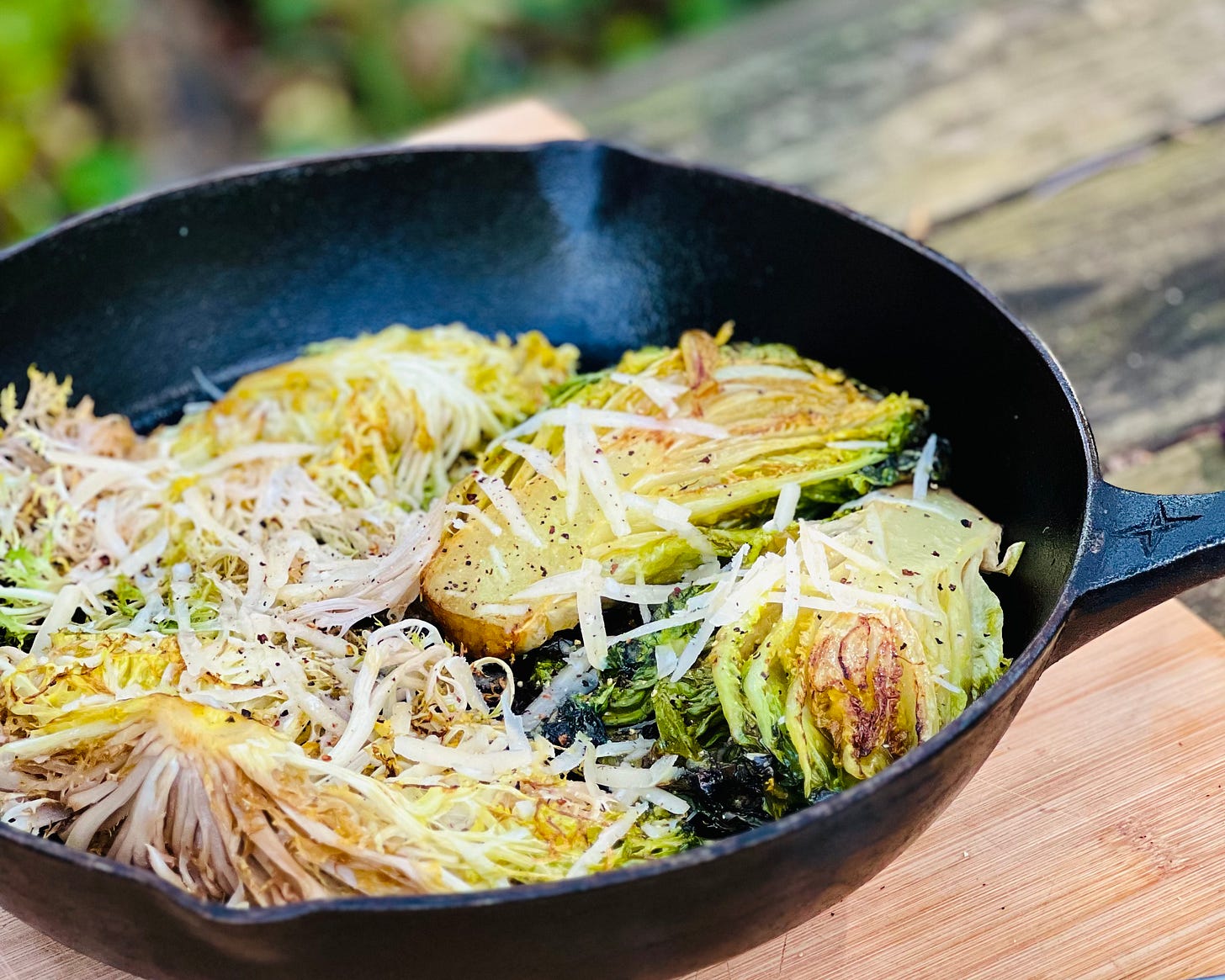 Pan-seared baby lettuce heads (gem and frisee) in a cast-iron skillet with shredded parmesan and black pepper over top