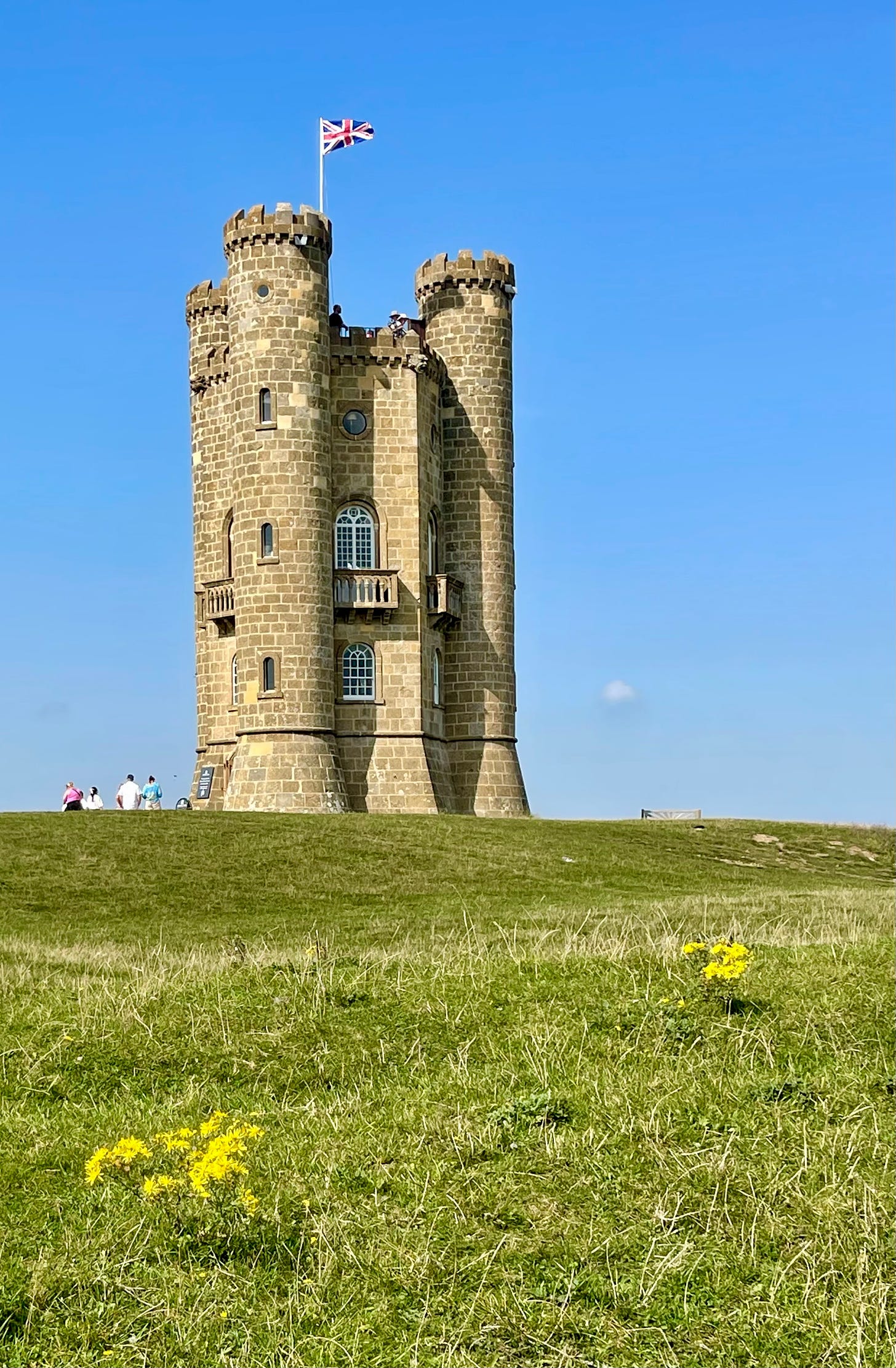 The Broadway Tower on the green grass of Beacon Hill against a bright blue sky in Worcestershire, England