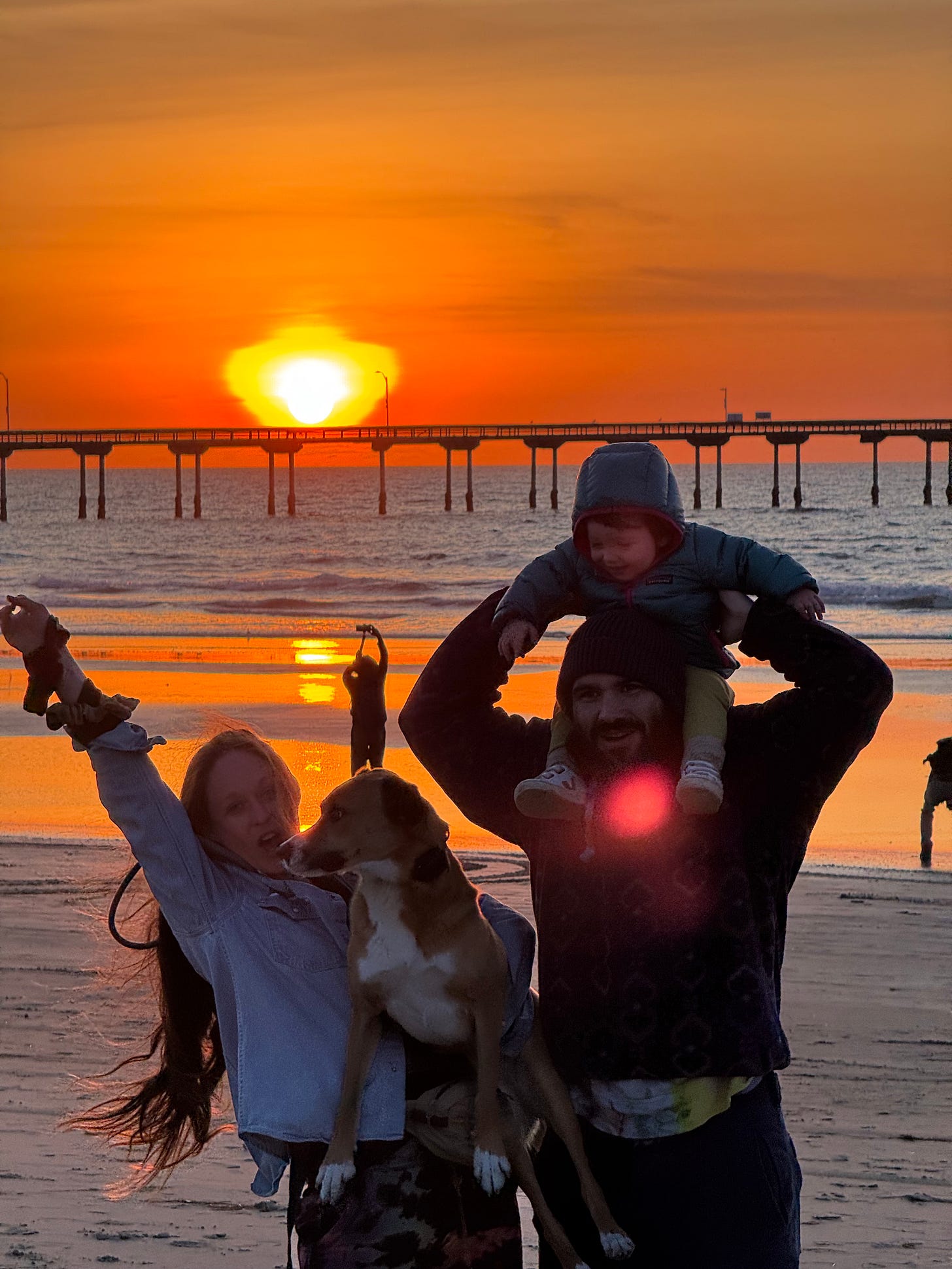 ferraro family on the beach with the OB pier behind them at sunset with a bright orange sun setting