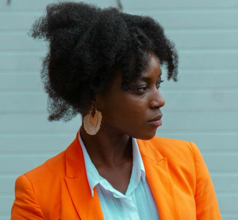 woman wearing orange blazer standing near white wall woman wearing orange blazer standing near white wall