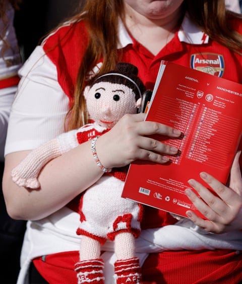 An Arsenal fan with a knitted doll and match programme at the WSL match between Arsenal and Manchester City at Meadow Park.