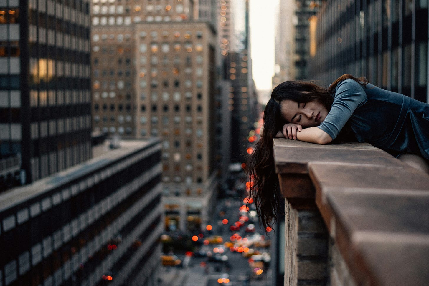woman resting on a city balcony overlooking busy streets below woman resting on a city balcony overlooking busy streets below