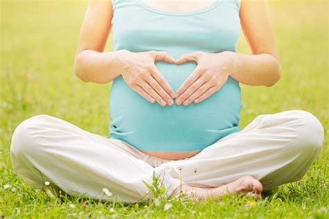 Woman holding her hands in a heart shape on her pregnant belly - Rising ...