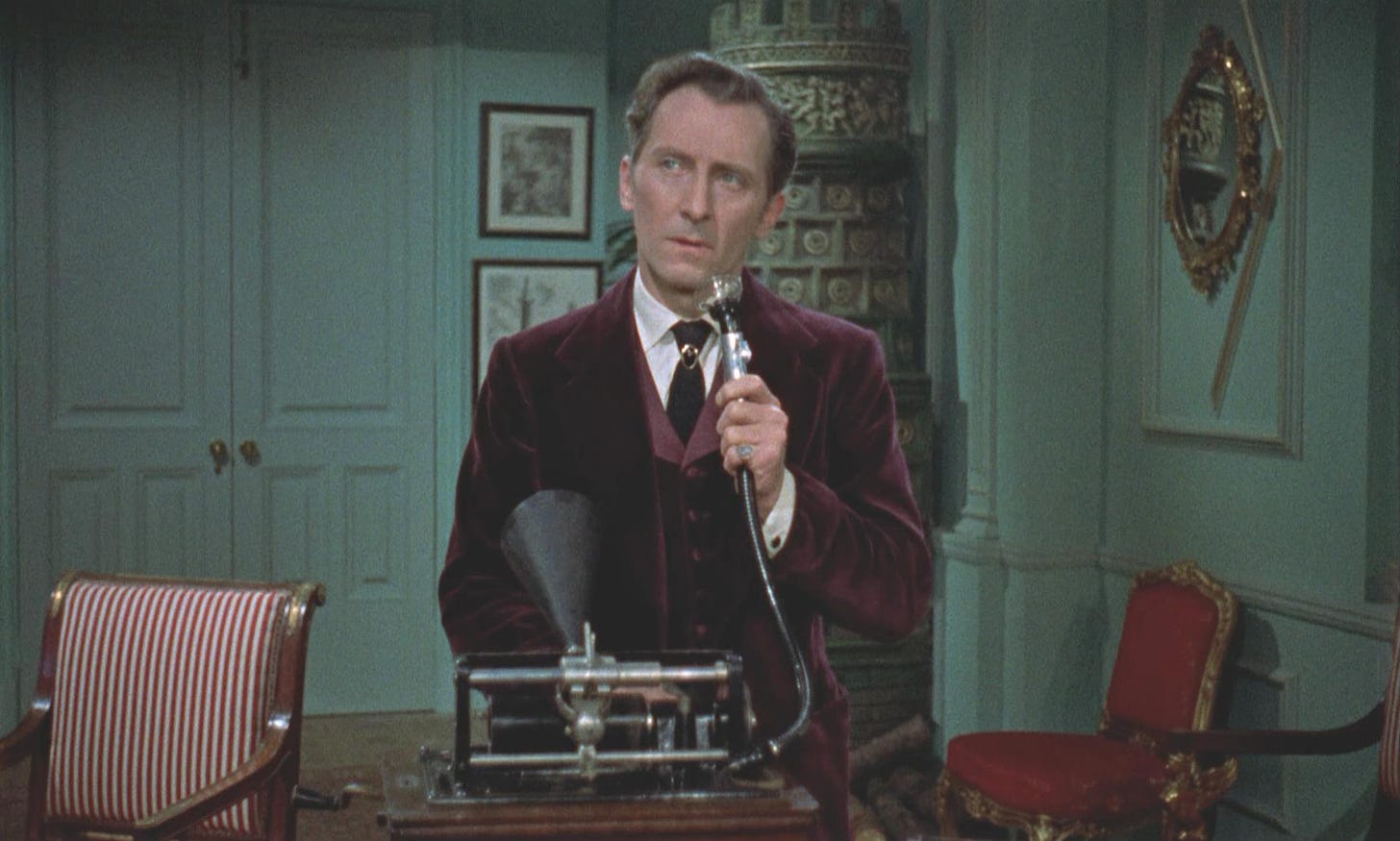 A man in a maroon crushed velvet jacket answers an old timey telephone.