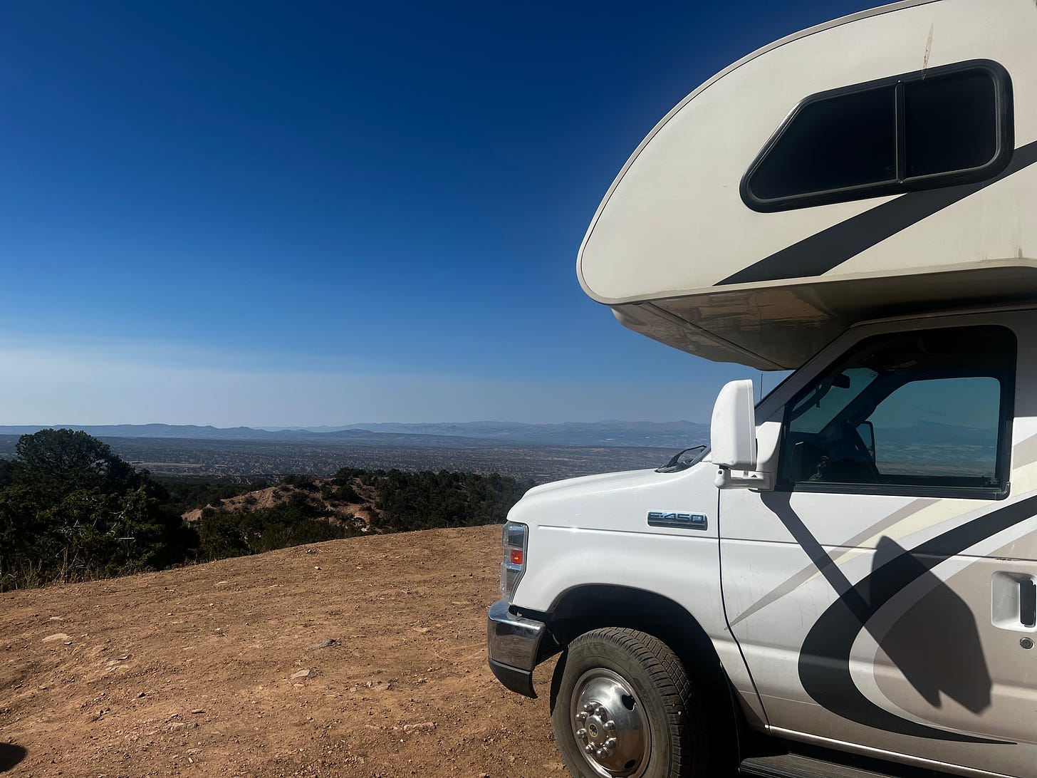 Photo of the front part of a tan and white RV on a Ford E450 van sitting on top of the SantaFe Mountians in NM