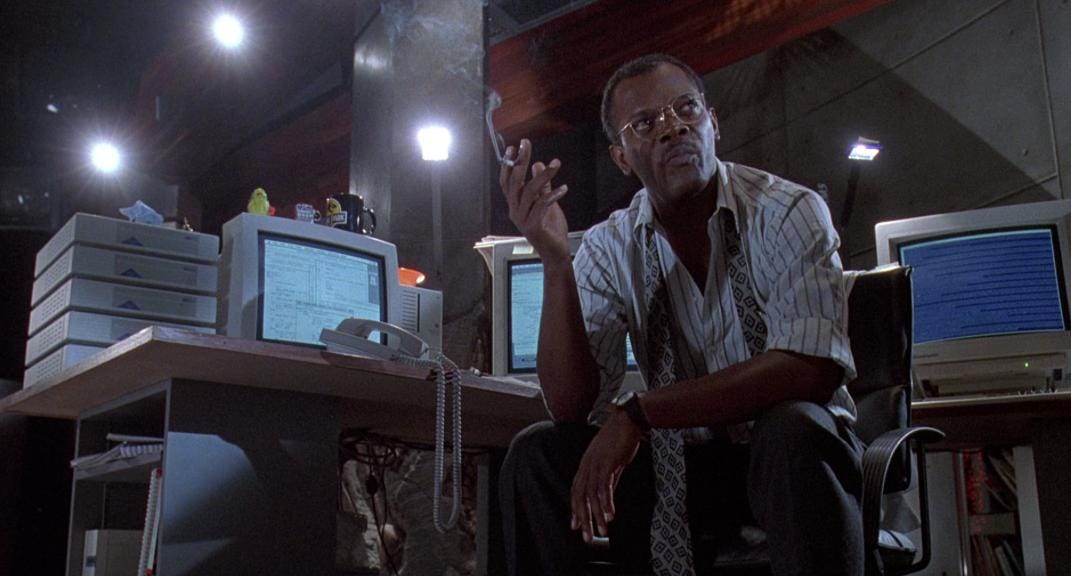 Samuel L. Jackson, smoking at his computer station in the Jurassic Park control center. He is tired of this hacker crap.