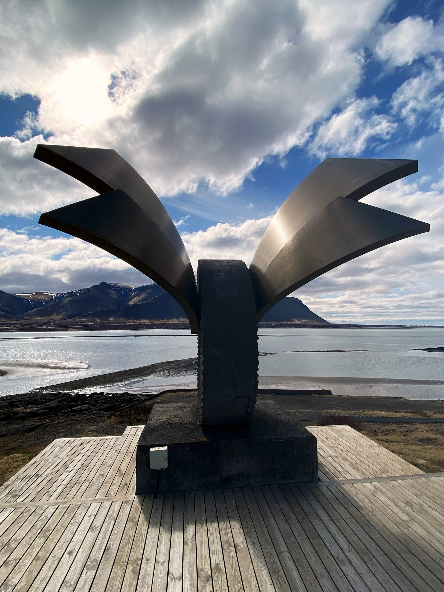 A sculpture with double steel wings extending from a curved ram's horn carved from stone overlooking the water in Borgarnes, Iceland.