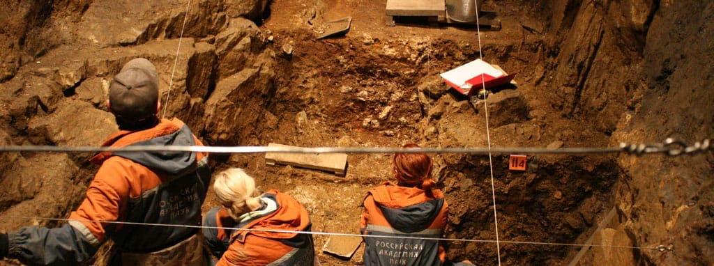 Three archaeologists working in brown sediment layers with records and tools around them