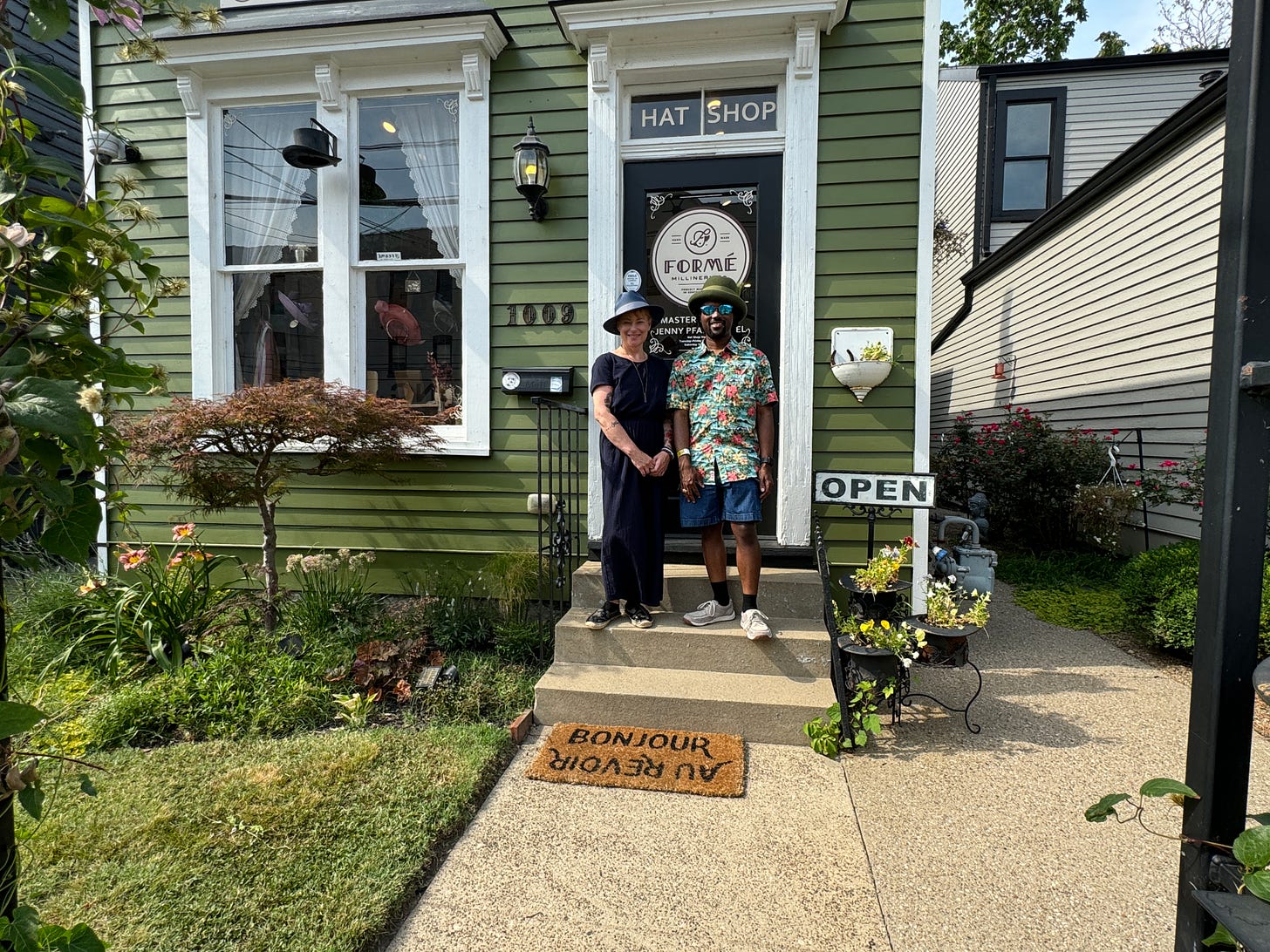 This is an image of Master Milliner Jenny Pfanenstiel and ArmaniXR wearing their hats outside of the Formé Millinery.