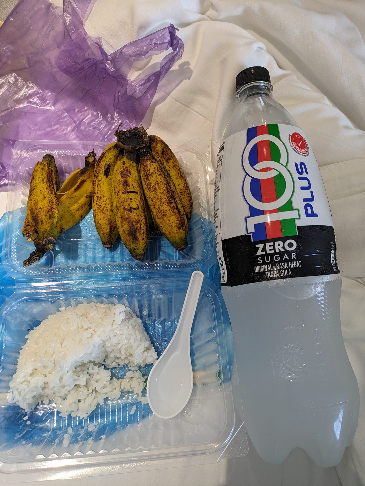 a take-out container of plain white rice, plus a cluster of small bananas and a large bottle of a sports drink