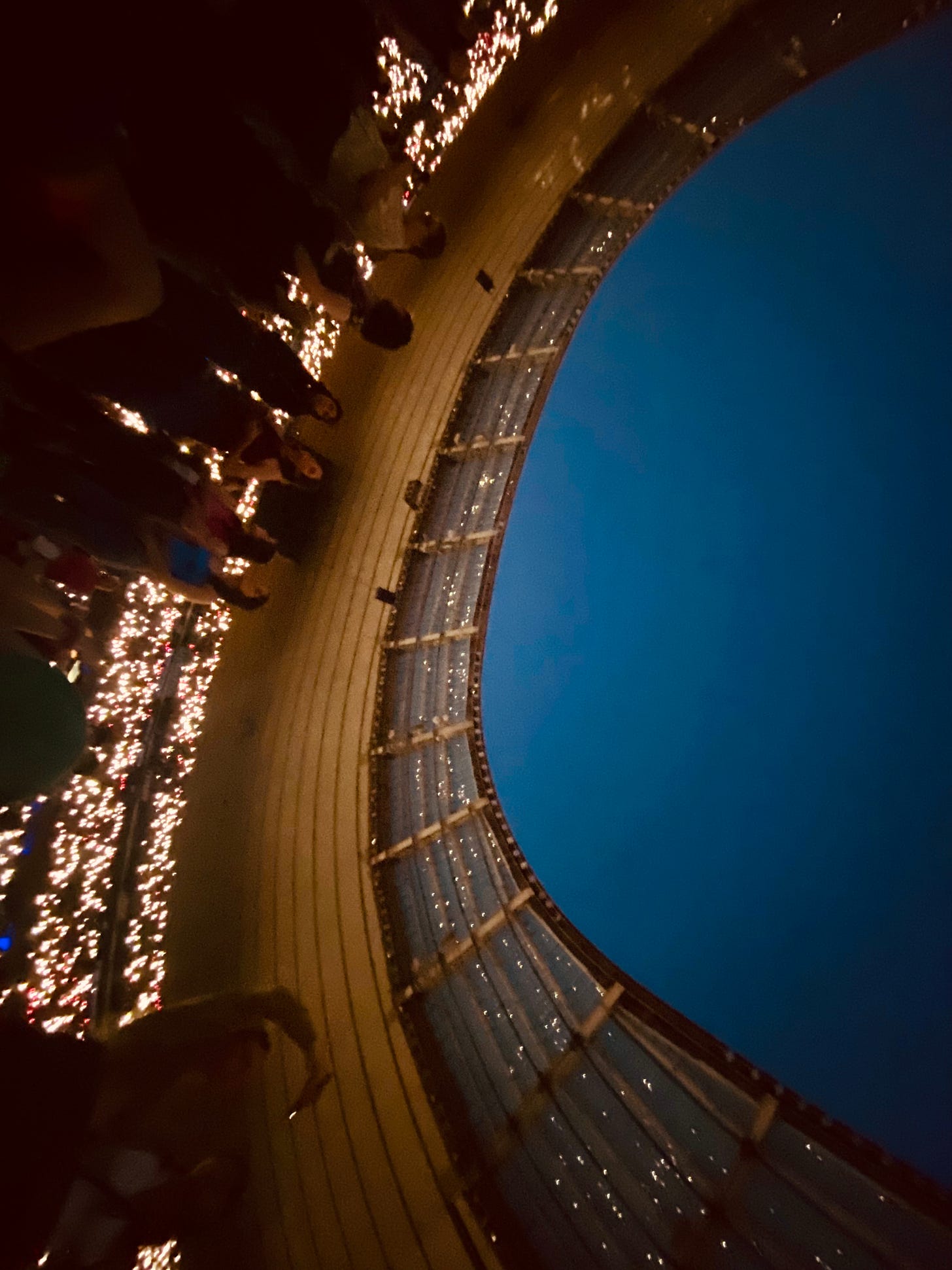 The blue night sky above the stadium and the lights from the fans' phones in the stands and reflected in the partial roof
