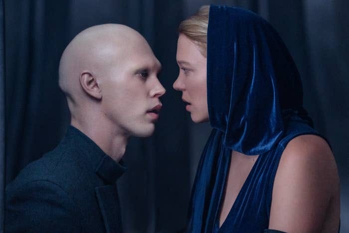Two characters in close conversation, one with a bald head, the other in a blue hooded garment