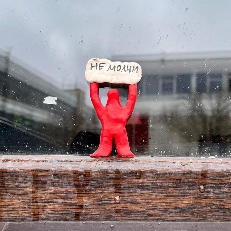 A red figurine in a window holds a white sign with the inscription “Don’t be silent” in Russian.