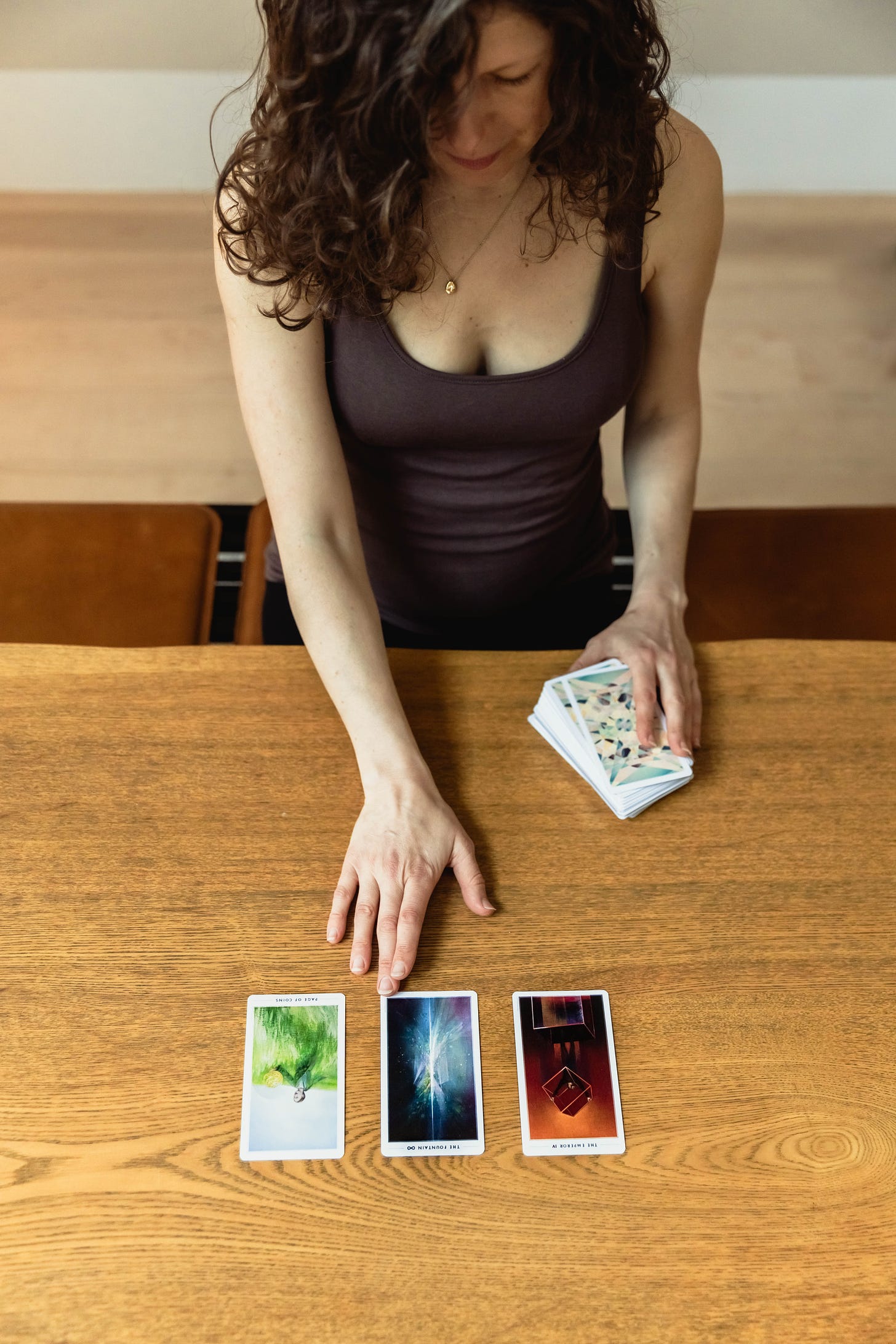 Woman seen from above with three tarot cards in front of her on a wooden table top