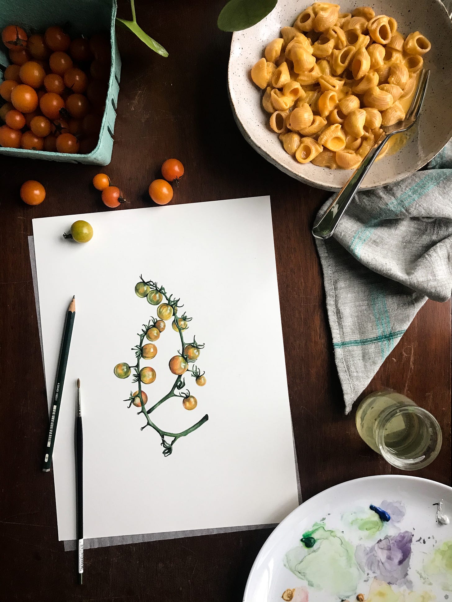 An image of a painting of sungolds on a wooden desk surface, with fresh sungold tomatoes spilling out in the top left corner, and a bowl of pasta with sungold sauce over it, a fork sticking out and a tan and blue striped napkin to the right of it. A pencil and paintbrush sit on the white of the paper. 