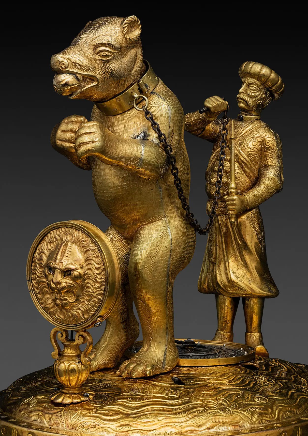 Bronze figures. A standing bear has a collar and chain and is being controlled by an opulently dressed man