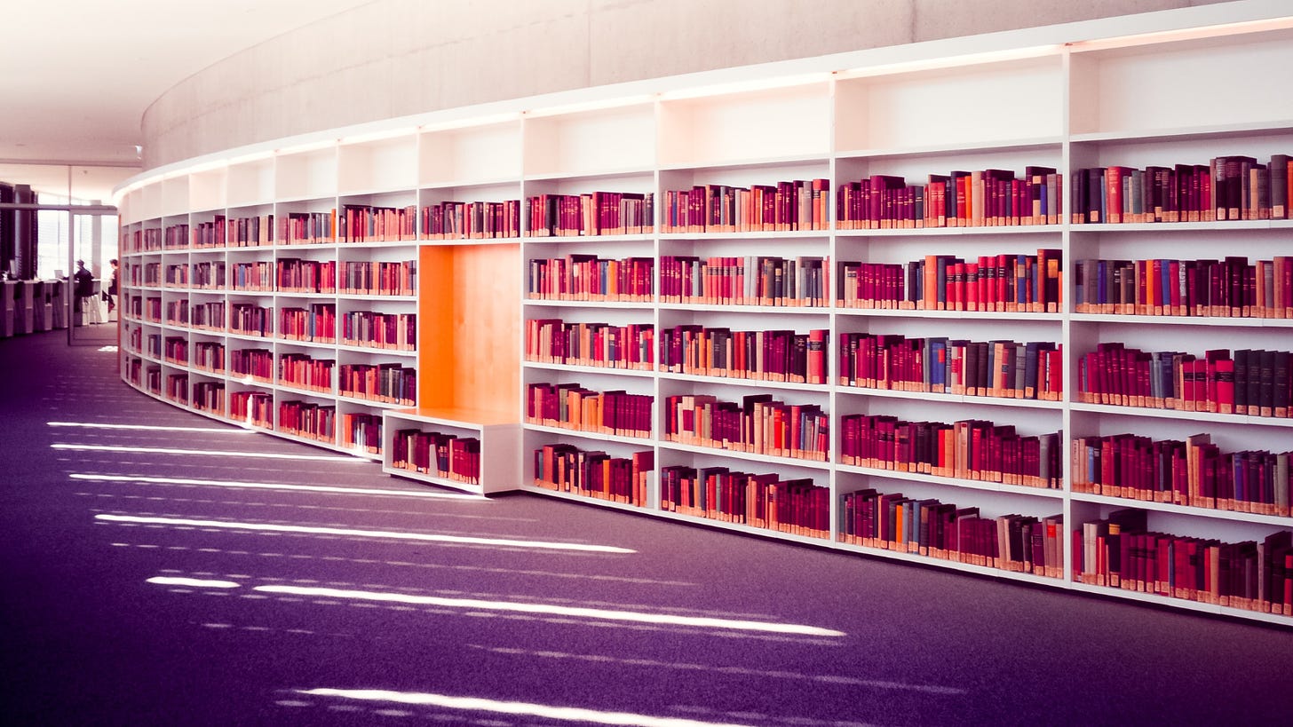 A golden-hour-filtered photo of a curved white library wall full of orange books, with purple carpet in the foreground