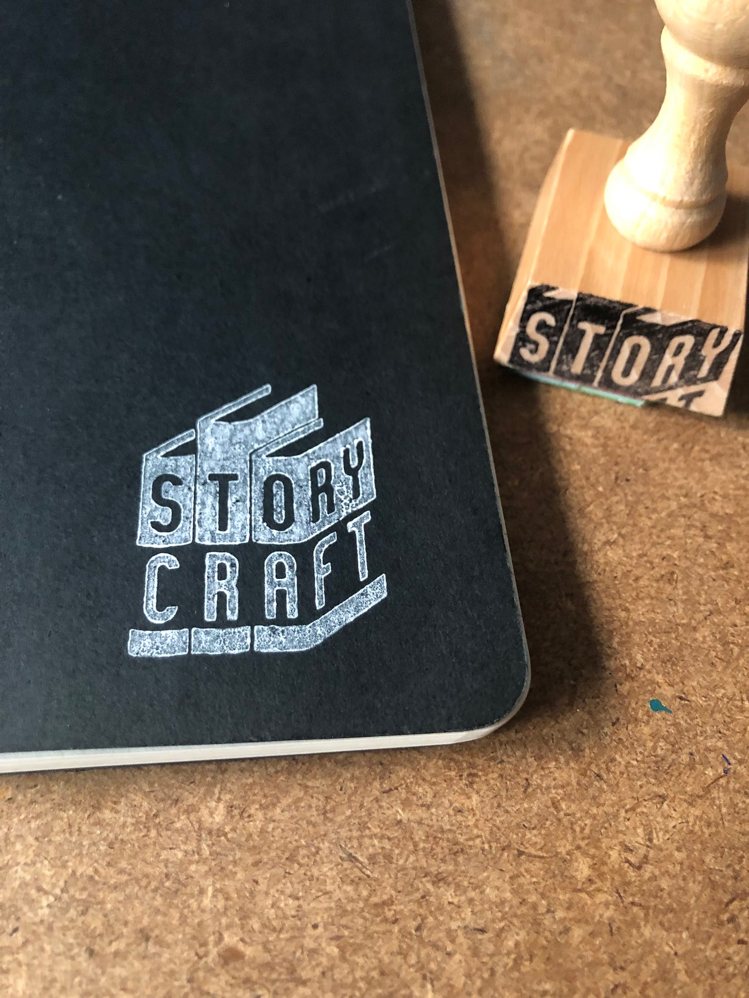Black notebook with a white Storycraft stamp next to a wooden Storycraft stamp.