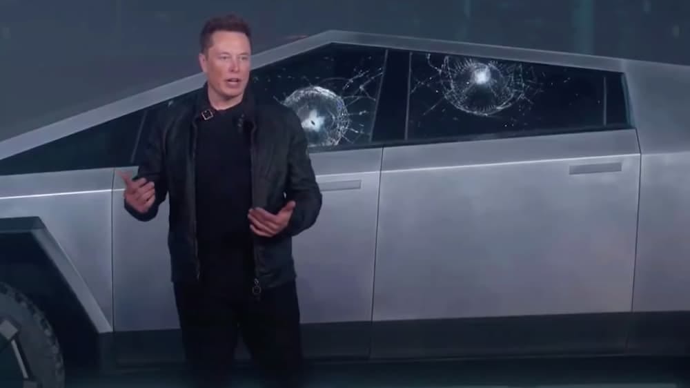 Elon Musk stands in front of Tesla's Cybertruck, which has two broken windows