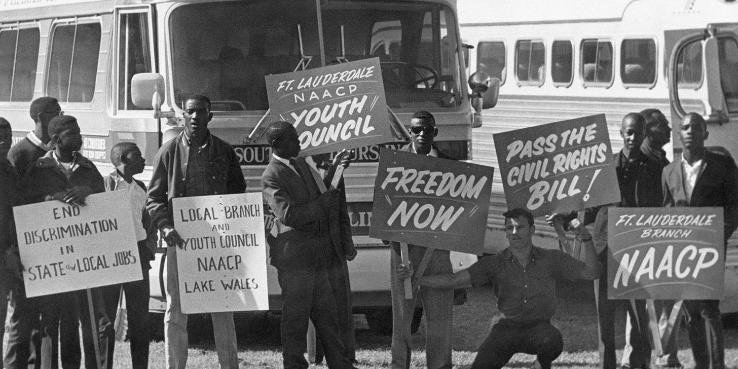 Marchers and members of the NAACP holding signs gather at a school athletic field in Tallahassee, Florida before a civil rights march.