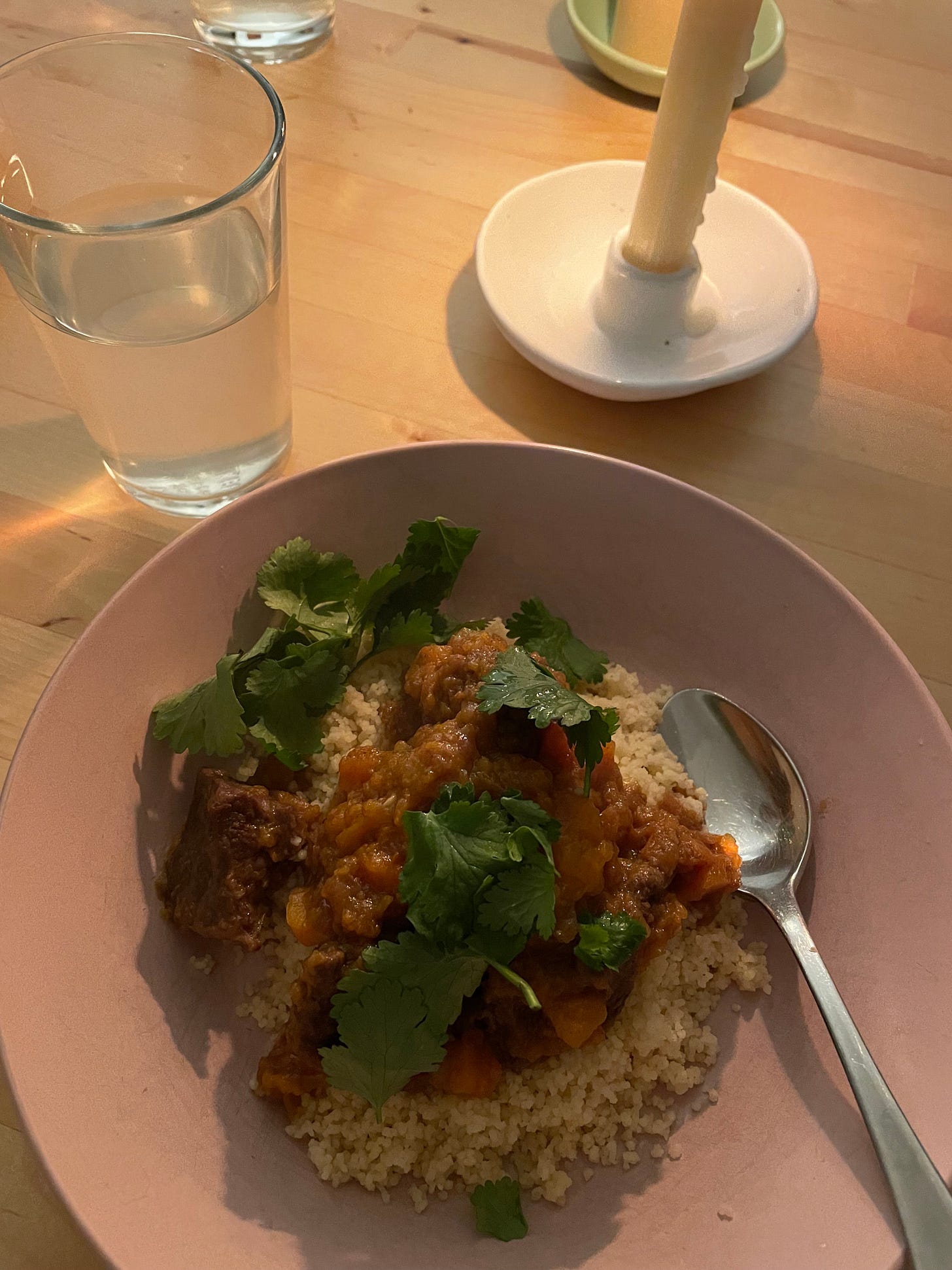 Bowl of beef stew with sweet potato sitting atop couscous and topped with coriander.