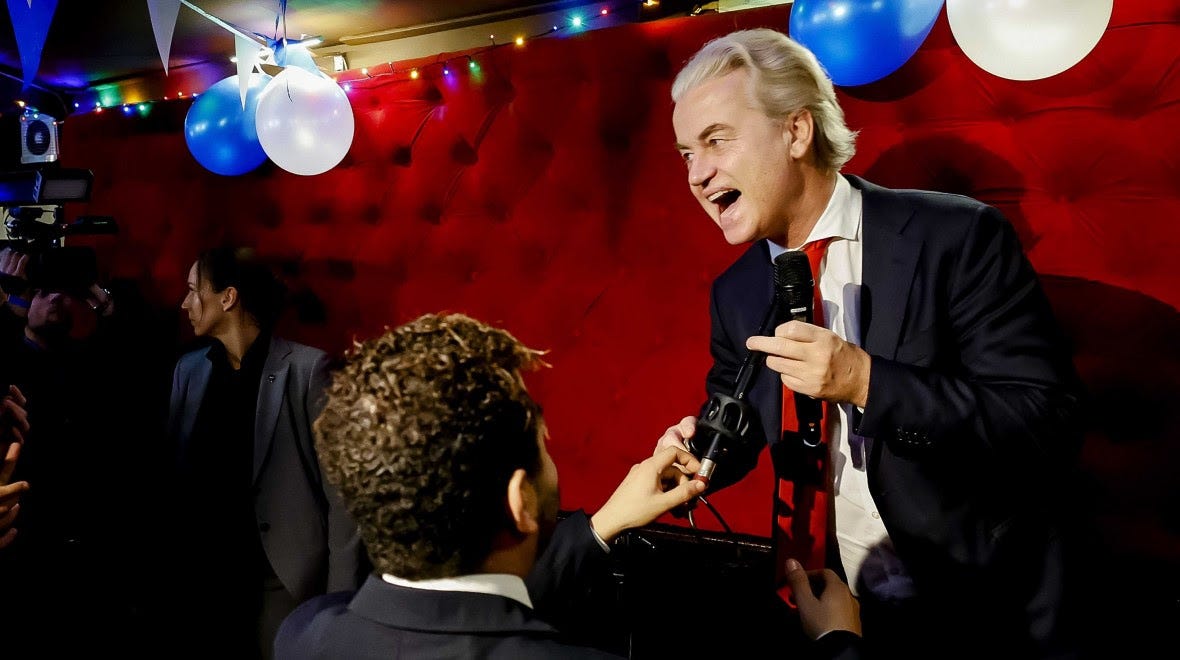 Geert Wilders smiles as he stands on a small stage as he reacts to electoral results.