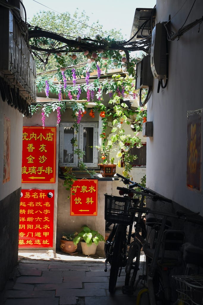 Fotografia di una casa all'interno di un Hutong di Pechino, con un glicine viola e dei cartelli con scritte gialle a sfondo rosso