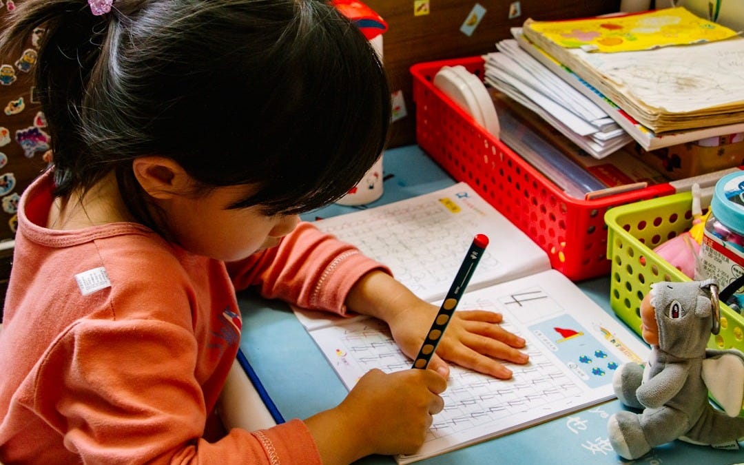 girl in orange long sleeve shirt writing on white paper girl in orange long sleeve shirt writing on white paper