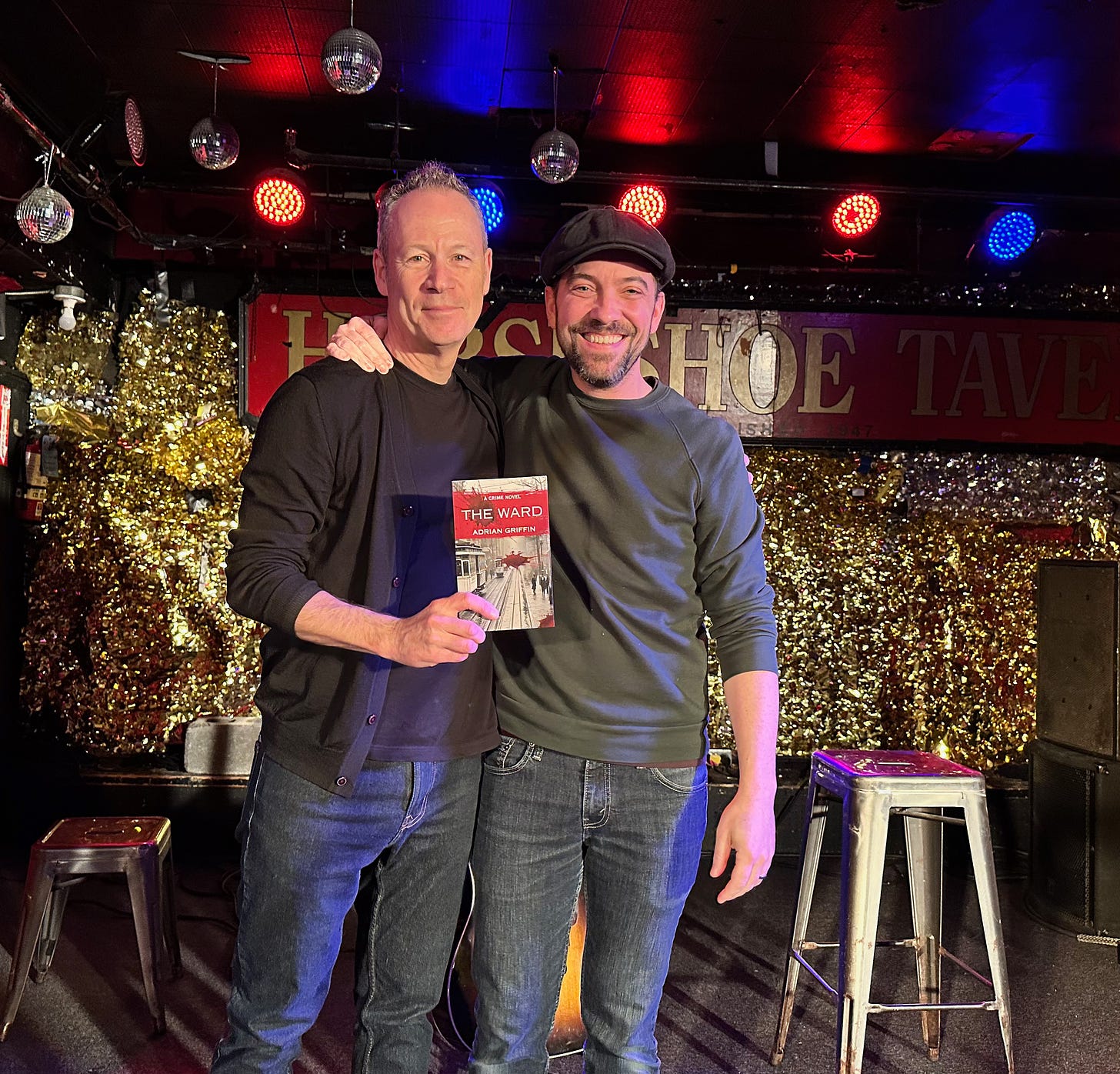 Adrian Griffin and Justin Rutledge posing with Adrian's novel onstage at the Horseshoe Tavern, Toronto