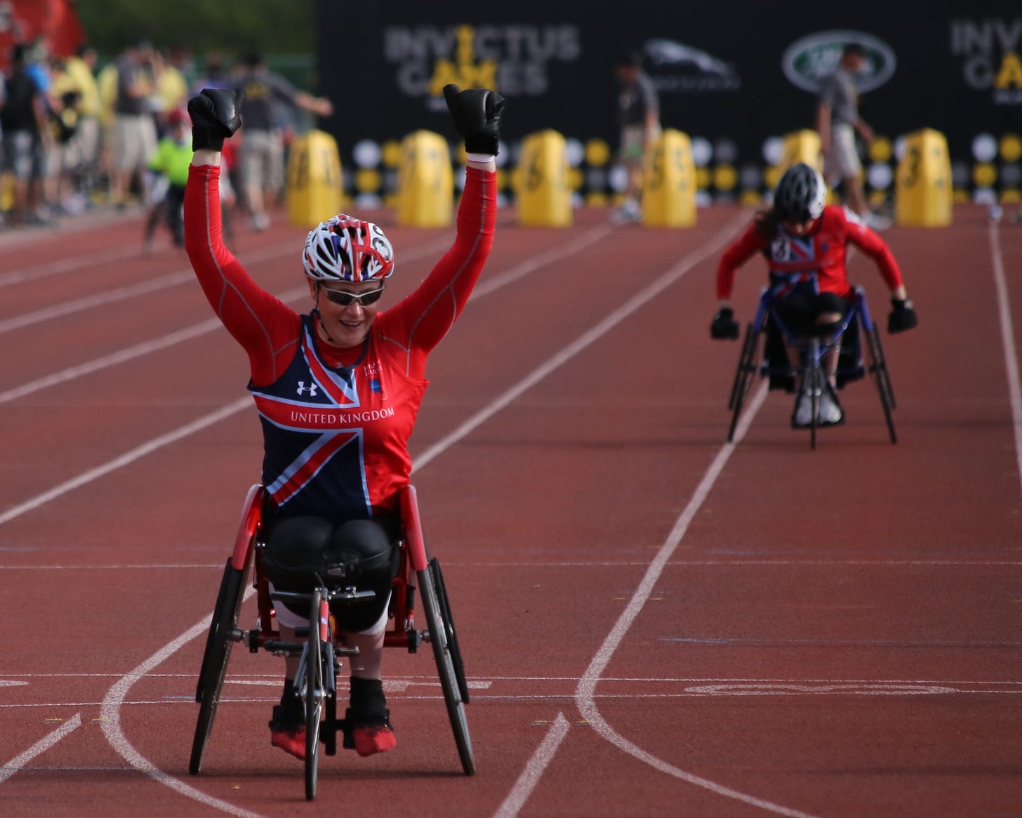 Photo of the end of a wheelchair race; close up of one racer raising their arms in celebration.