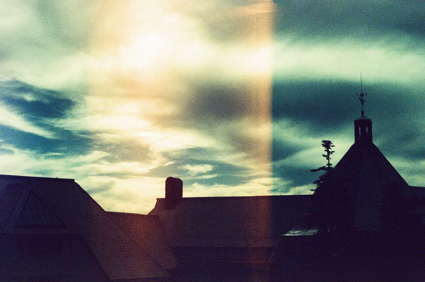 A film photo of darkened buildings below a bright sky.