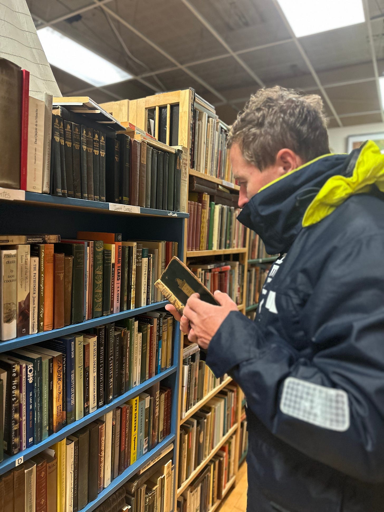 A man in rain gear is leafing a used book in a bookstore
