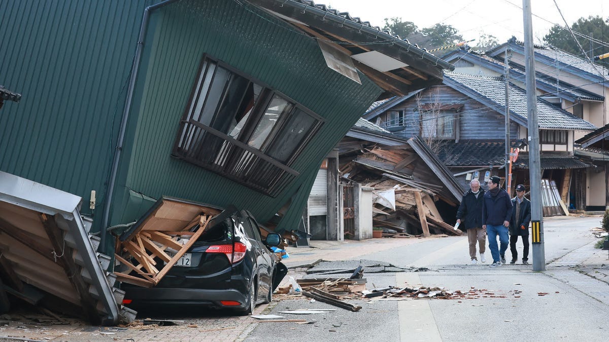 People walk past a badly damaged house in the city of Nanao, Ishikawa Prefecture, Japan, on January 2, 2024, a day after a major 7.5 magnitude earthquake struck the region.