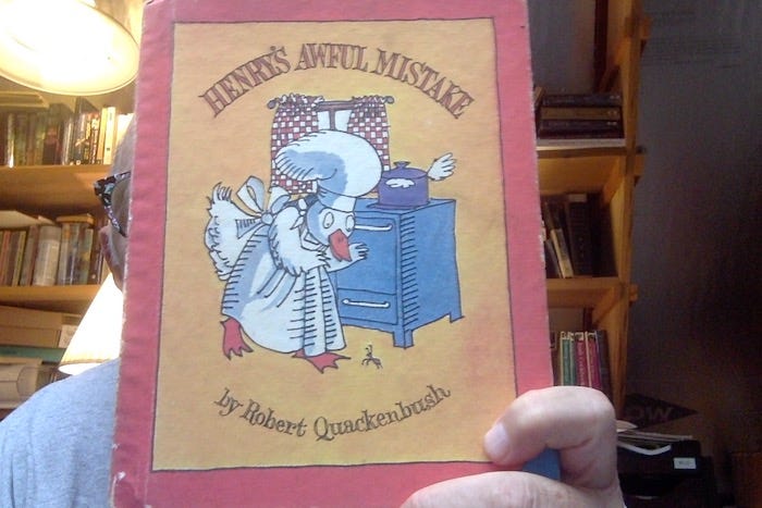 Photo of me holding my copy of Robert Quackenbush's "Henry's Awful Mistake". On the cover, a white duck, whearing a white apron and a white chef's hat, standing before an old fashioned stove, looks t the floor, where there is an ant.