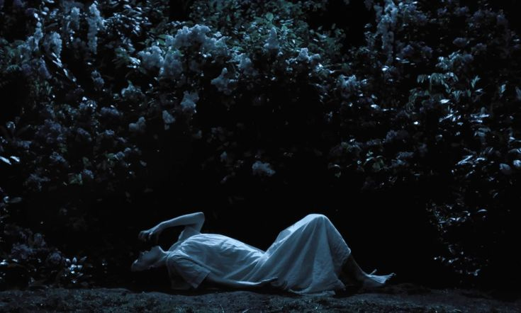 This may contain: a woman laying on the ground in front of trees at night with her head down